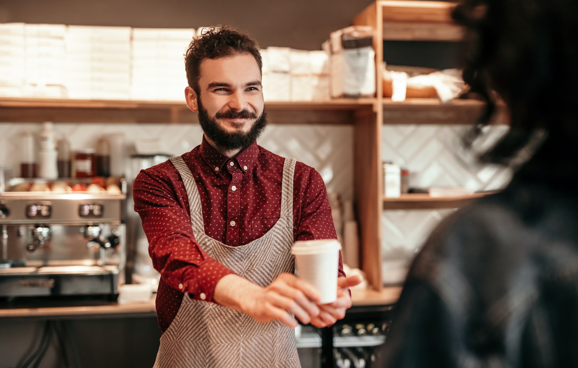 Cheerful bartender suggesting disposable cup with drink to client